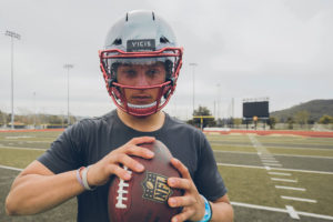 1UP Sports Marketing client Patrick Mahomes in a tee holding a football and wearing a football helmet