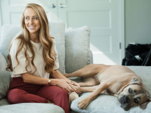 1UP Sports Marketing client Brittany Lynne Matthews smiling while sitting on the couch next to her dog