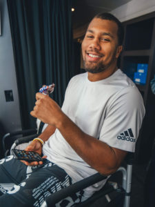 1UP Sports Marketing client Bradley Chubb sits in a chair holding a Snickers bar with the wrapper torn