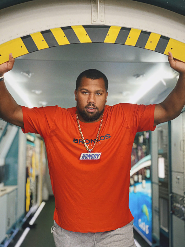 1UP Sports Marketing client Bradley Chubb poses in a doorway with a Snickers "Hungry" chain and pendant