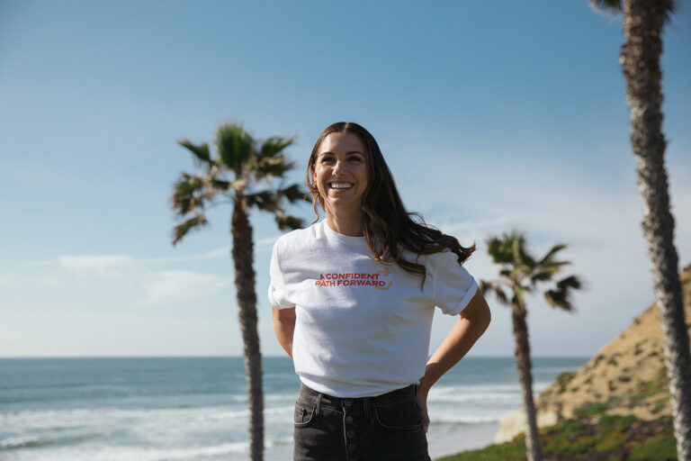 1UP Sports Marketing client Alex Morgan smiling and wearing a "Confident Path Forward" tee shirt