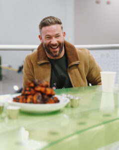 1UP Sports Marketing client Julian Edelman sitting in front of a plate of chicken wings