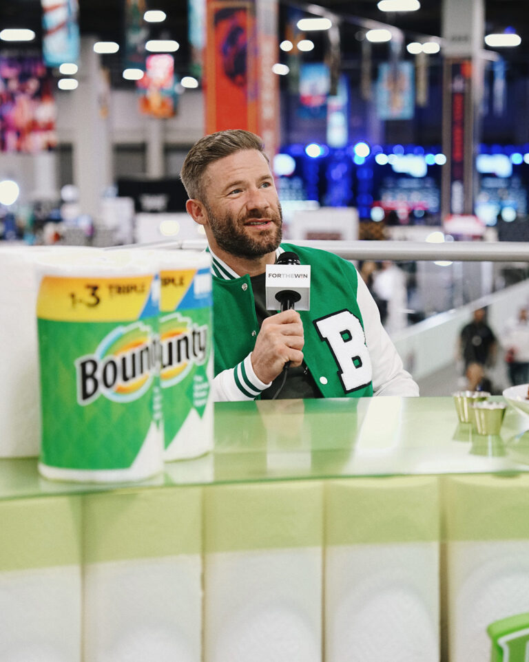 1UP Sports Marketing client Julian Edelman using a microphone sitting in front of several rolls of Bounty