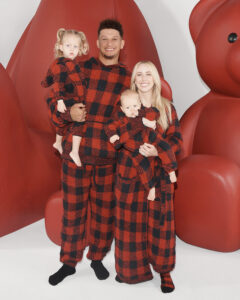 1UP Sports Marketing clients Patrick and Brittany Mahomes stand and hold kids in red and black checkered onesies by SKIMS