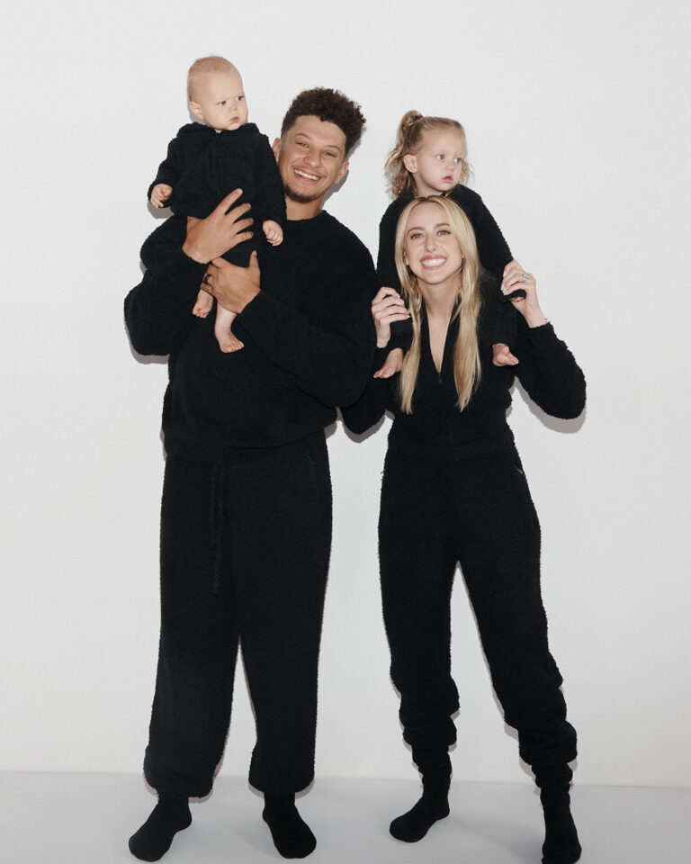 1UP Sports Marketing clients Patrick and Brittany Mahomes smile while holding their kids in black onesies by SKIMS